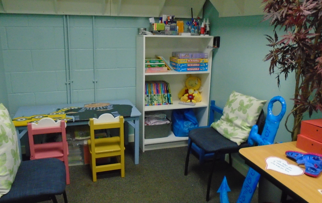 A small blue room with a desk, office chair and noticeboard, a children's bookcase and a children's table and chair
