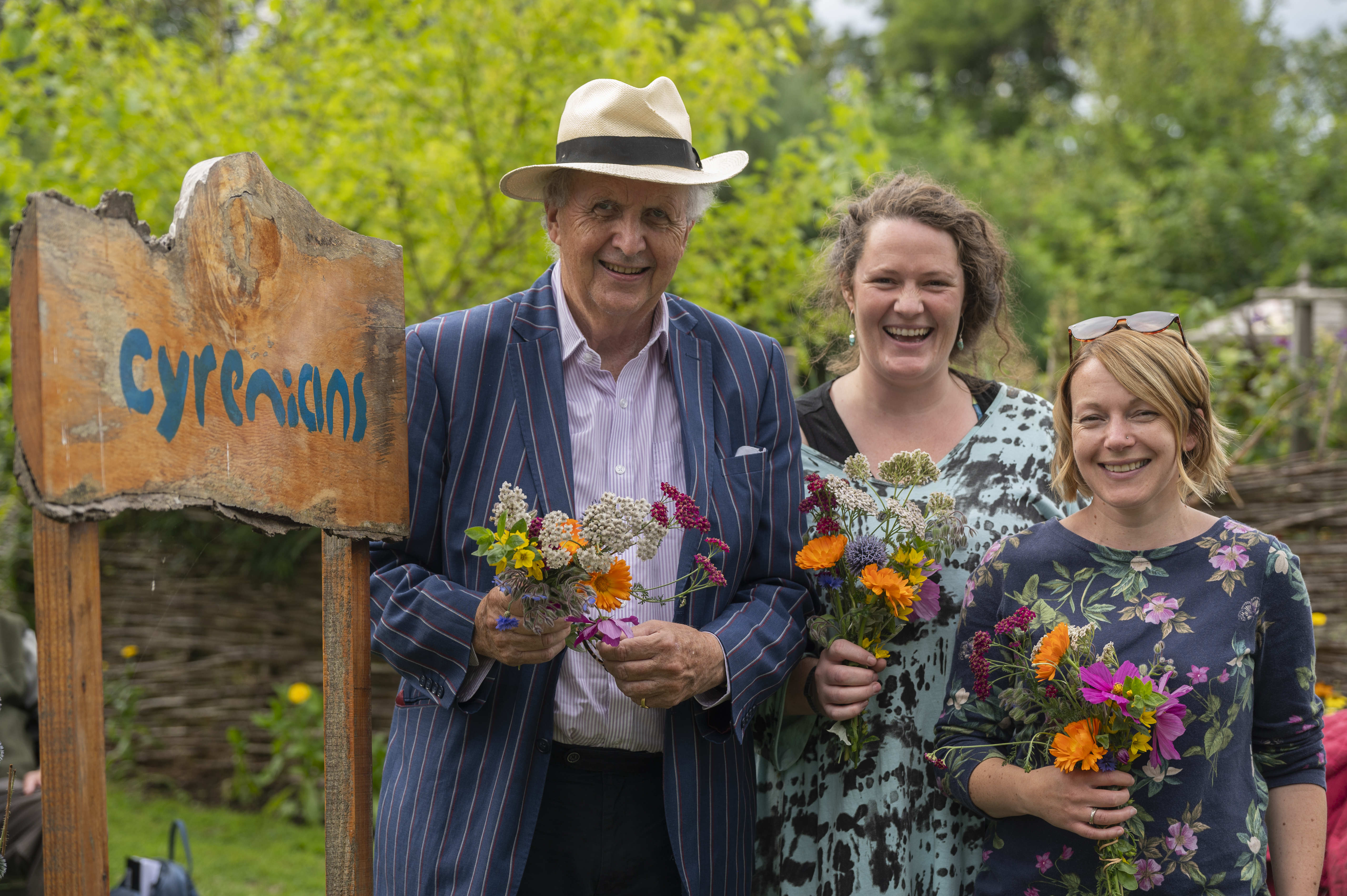 Alexander McCall Smith and Cyrenians Gardens staff Hannah MacRae and Lucy Gilroyd hold flowers by a sign reading Cyrenians (photo: Phil Wilkinson, 2023)